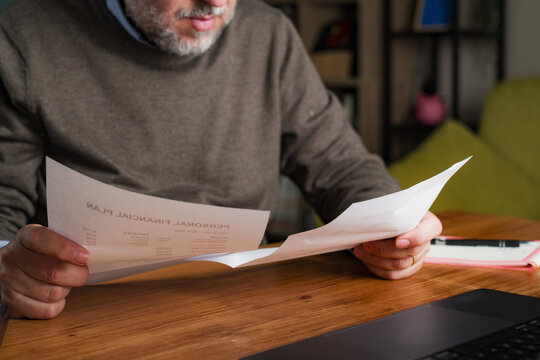 Mature man comparing financial documents at home making budgeting decision
