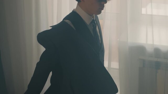 Asian musician adjusting cufflink before performance with soft window light, formal vest and suit, chair with jacket draped, quiet backstage ritual, focused preparation and subtle tension captured