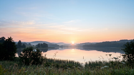 Fototapeta premium Serene misty lake at sunrise with forest reflection on water surface