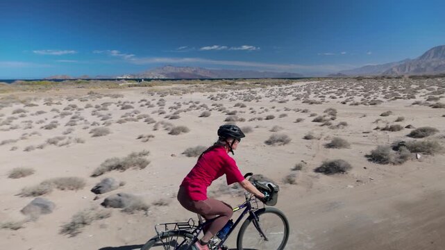 A senior woman enjoys biking along Bahia De Los Angeles near La Gringa on a sunny day by the Sea of Cortez in Mexico.