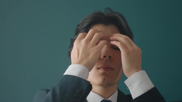 Young male executive styling hair, pulling hair back into tidy bun while rehearsing pitch, studio teal backdrop and tailored suit convey founder energy and growing confidence before meeting.