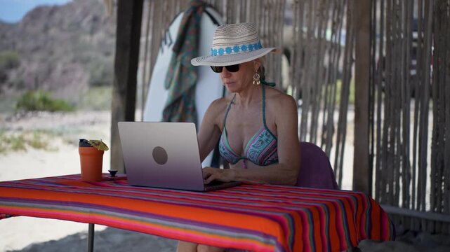 Mature woman works on her computer at a tropical beach and shows various emotions while enjoying her vacation.