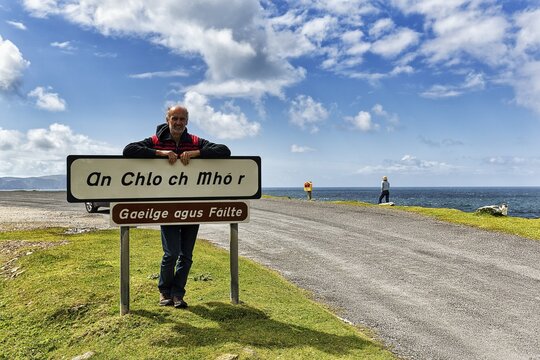Tourist leaning against welcome sign in Irish, inscription Gaeilge Agus Failte, panoramic Atlantic Drive, southern Achill Island, Mayo, Wild Atlantic Way, Ireland