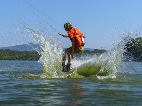 Young casual man with flapping shirt on wakeboard jumping into the lake, water ski and wakepark, Str&aacute;ž pod Ralskem, Czech Republic