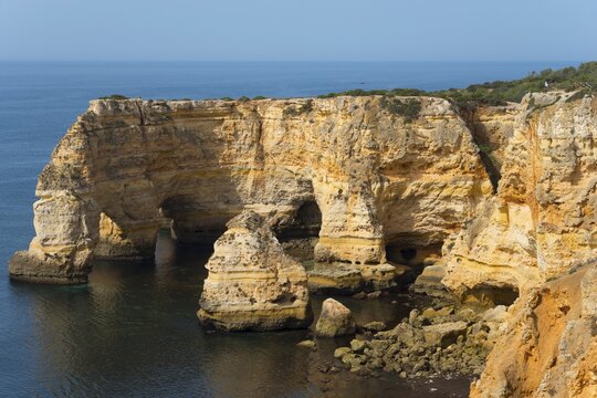 Steep cliffs and craggy rocks jut out of the calm sea on a clear day, Praia da Marinha, Lagoa, Rocky Algarve, Algarve, Portugal