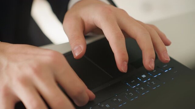 Closeup hands typing laptop keyboard in bright office, calm professional in suit preparing report, measured keystrokes and deliberate pace, natural daylight on desk, focused meeting prep