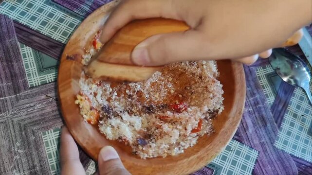 Grinding fresh chili, palm sugar, and shrimp paste in a traditional wooden mortar to make Indonesian sambal.