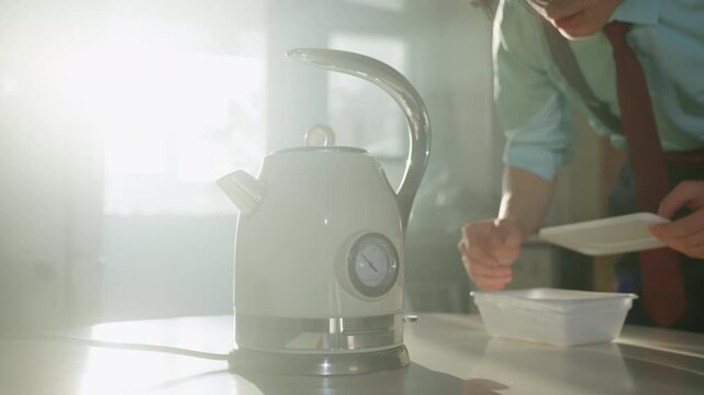 Kettle on sunlit countertop asian barista hands prepare tea, measuring water at gauge, placing ceramic container into package, warm backlight and soft steam, vintage stainless design, calm morning