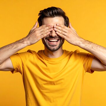 A man covering his eyes with a wide smile on a yellow background