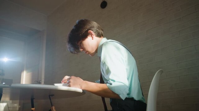 Asian student slumped over desk, lamplight casting warm glow, pen in hand, papers scattered, suspenders and shirt, tense posture, bowed head, quiet exhaustion, solitary interior mood