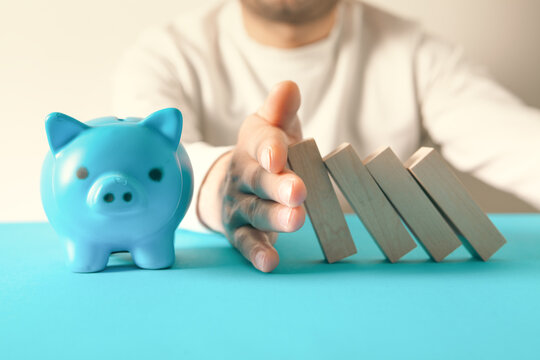 man hand with piggy bank and wooden dominoes on color background