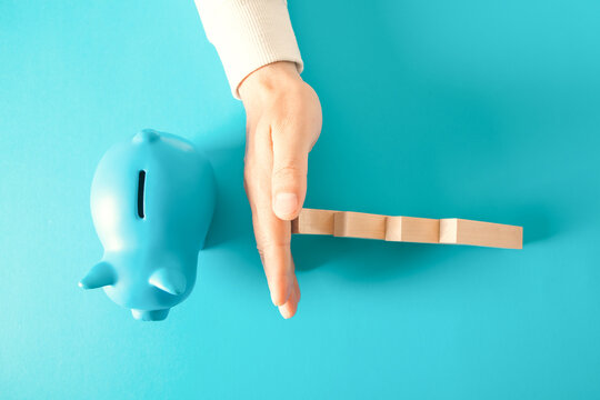 man hand with piggy bank and wooden dominoes on color background