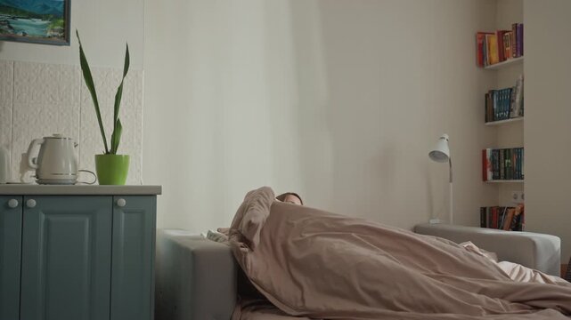White woman tucks into bed evening lamplight and bookshelf backdrop, green plant by cabinet music lover pulls duvet, settles into cocoon, closes eyes and drifts scene warm and intimate, cinematic