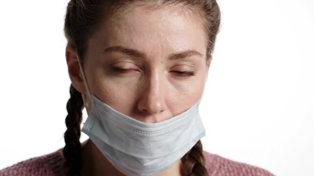 Closeup portrait of a young woman with braided hair wearing a medical face mask pulled down below her nose and mouth isolated on white background