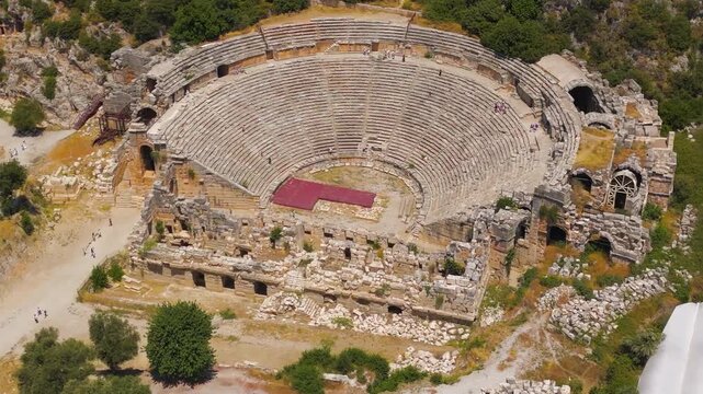 Demre, Turkey. Myra Roman amphitheater, sweeping aerial view over the 10,000-seat stone cavea and ruined scaenae frons carved into the hillside under bright summer sun. Aerial View, MasterShots, Circ