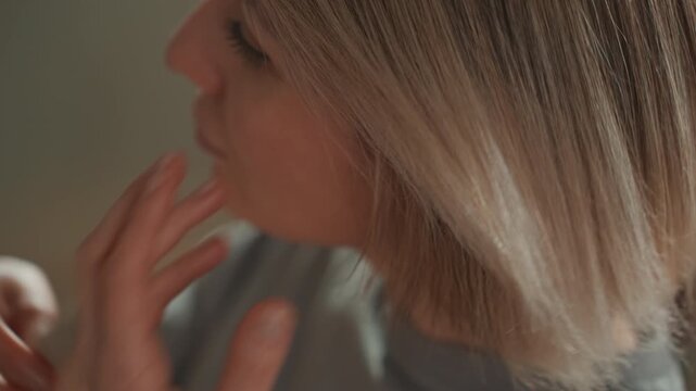 Caucasian woman music lover adjusting bob athome closeup, hands tucking blonde hair behind ear, soft warm lighting, cozy sweater, contemplative expression, cinematic bokeh, intimate grooming moment