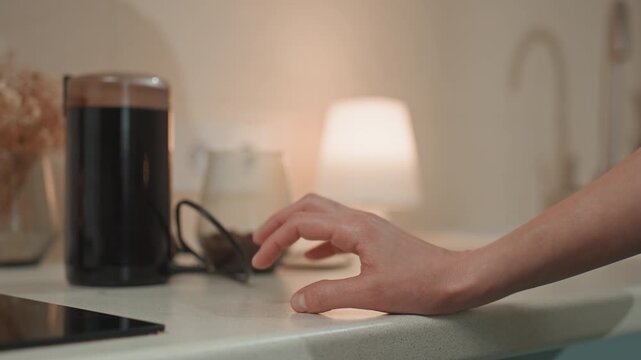 White woman fingers tapping kitchen counter under warm lamp glow, coffee press and glass jar visible in background, fingertips play gentle rhythm like soft melody, closeup hand gestures convey romance