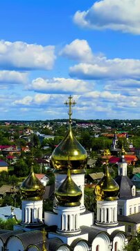 Vertical video. Pereslavl-Zalessky, Russia. St. Nicholas Pereslavsky Monastery, golden onion domes and white walls, Drone footage over the historic Golden Ring town under a partly cloudy summer sky. 