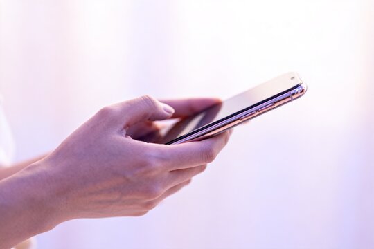 Hands Holding Rose Gold Smartphone Against Soft White Background