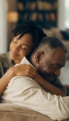 Obraz premium Young Black Woman Hugging Senior Black Man From Behind on Couch in Warm Home Interior Tender Father and Daughter Embrace on Fathers Day Family Love Bonding Concept