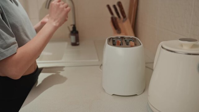 Person placing toast into toaster morning kitchen, cropped torso and hands, casual shirt, kettle and utensils on counter, upbeat rhythm vibe, music playing, playful domestic moment, quick breakfast