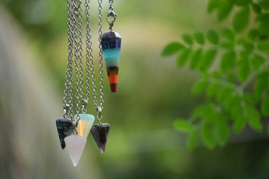 Several crystal pendulums, including a colorful chakra one, dangle beautifully near green leaves.