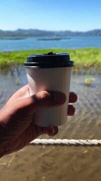 Hand holding a paper cup of coffee with beautiful landscape background. 4K Vertical Video Format