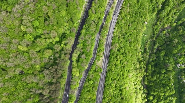 Cinematic top view drone footage of winding mountain highway and green forest with moving cars 4K.