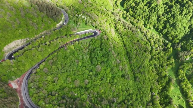 Cinematic top view drone footage of winding mountain highway and green forest with moving cars 4K.