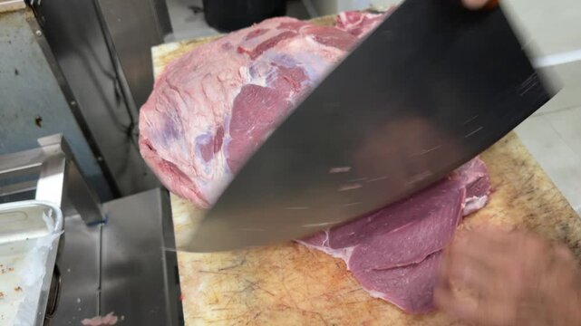 Butcher skillfully slicing a large piece of beef with a cleaver
