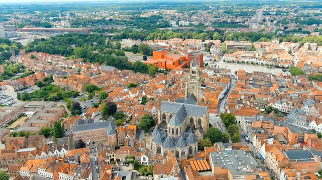Bruges, Belgium. Church of Our Lady - Gothic church from the 13th century. Panorama of the city center from the air. Cloudy weather, summer day. Drone footage, Departure of the camera