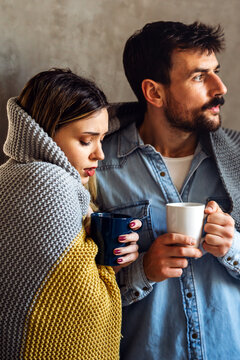 Freezing couple covered with a blanket. Man and a woman wrapped in a warm blanket in a cold room.