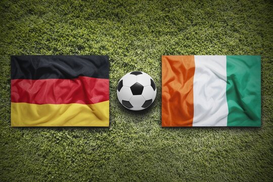 German and Ivorian flags flank a soccer ball on a lush green turf, symbolizing a sports match
