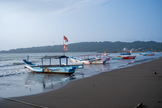 Cilacap, Indonesia - May 13, 2026: Traditional wooden outrigger fishing boat resting on the shoreline of Teluk Penyu Beach with Nusakambangan Island in the background.