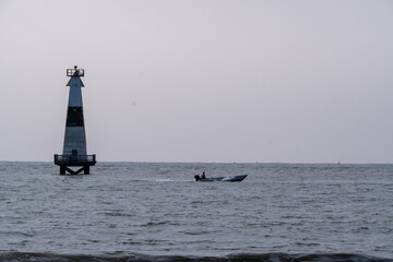 Fototapeta premium Small motorized boat passing an offshore lighthouse beacon on the calm morning sea in Cilacap, Indonesia.
