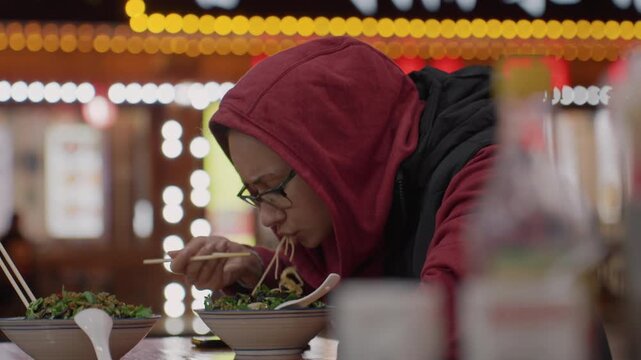 Asian woman slurping noodles under neon signs at night, solo traveler savoring street food with bottles in foreground, closeup of hands and chopsticks, cinematic bokeh lights and warm cozy atmosphere