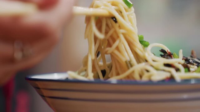 Closeup chopsticks lifting noodle strands from bowl, glossy texture and steam rising around scallion and seaweed garnish, energetic pull and slurp motion, hands guiding tangle, cinematic casual dining