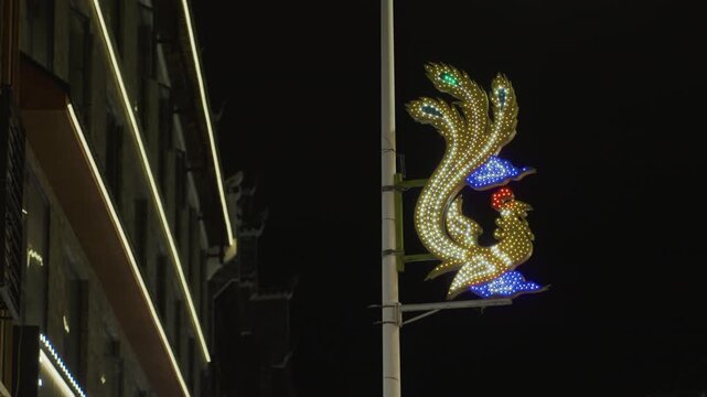 Night street with illuminated ornament golden decorative lights shaped like abstract crest attached to lamppost beside modern building facade blue and green accents quiet urban evening ideal for night
