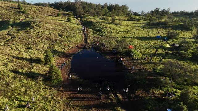 Aerial footage small lake in the meadow with a crowd of several hikers and tents.