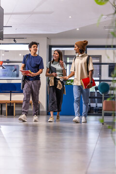Diverse students walking and talking in modern campus lobby holding notebooks and backpacks
