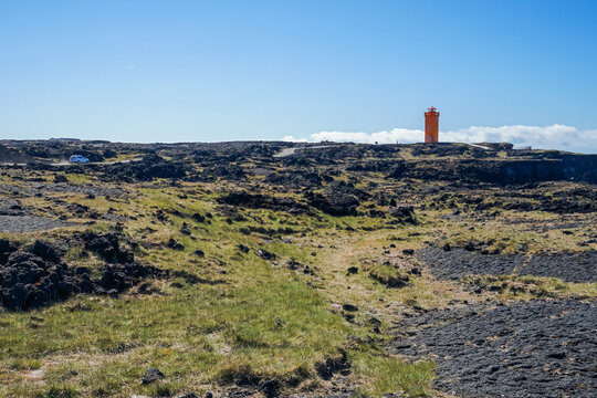 A barren landscape with sparse vegetation and a red tower in the distance under a clear blue sky,ICELAND