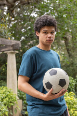 Naklejka premium Adult African man standing in green park holding black-and-white soccer ball near stone column