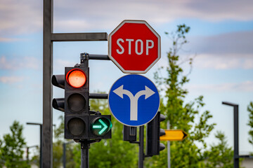 Stop sign, blue direction sign, and traffic lights at a modern city intersection with trees and sky in the background. © Studio Aurelia