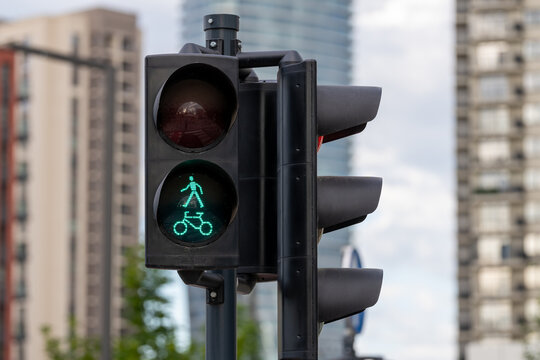 Close-up of a green pedestrian and bicycle crossing signal at an urban intersection with soft blurred buildings in the background.