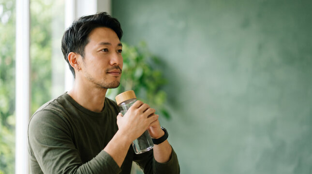 健康的な日常習慣の中でひと息つく30代日本人男性。
ユーカリグリーン背景が落ち着いたウェルネスイメージを演出。