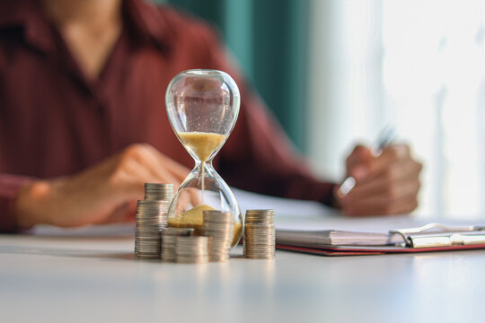Coin stacks and sand clock on the table. Growing of income, saving or return investment through time. Time and money concept.