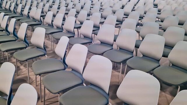Rows of empty modern grey and white chairs arranged in a large auditorium, conference room, or event hall. Concept of business meeting, seminar, or canceled public event