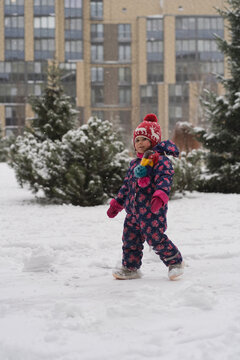 Little girl in floral snowsuit walking in snow looking at camera