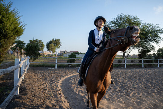 Young girl riding chestnut horse during equestrian lesson outdoors