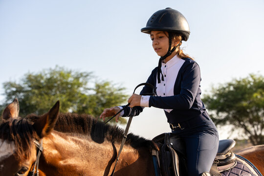Young girl riding bay horse during equestrian training outdoors